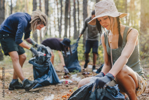 Young woman with group of activists cleaning forest of debri folding and plastic in bag
