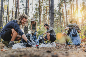 Multiracial group of volunteers taking care of nature ecology and picking garbage in plastic bags cleaning ground in forest