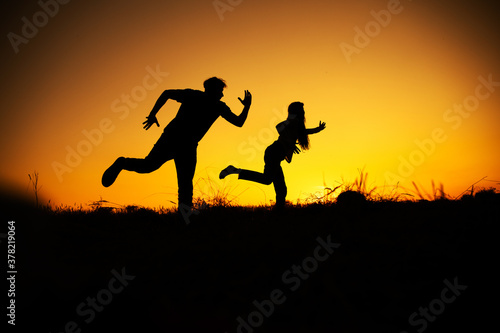 Young couple: man and woman run together on a sunset 