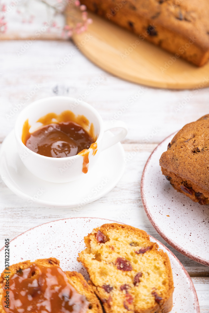 Homemade cake with raisins, almonds, soft caramel and a cup of coffee on a white wooden background. Side view, selective focus. Homemade cake with raisins, almonds, soft caramel and a cup of coffee on a white wooden background. Side view, selective focus.
