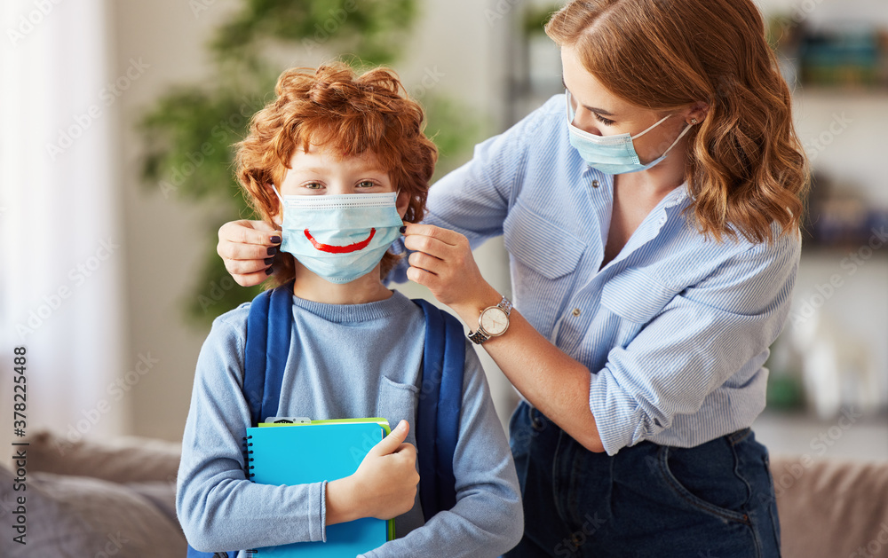 Concept of preventing a coronavirus covid-19 and viral infections. Mother puts on medical mask with painted smile for   son before leaving home for school.