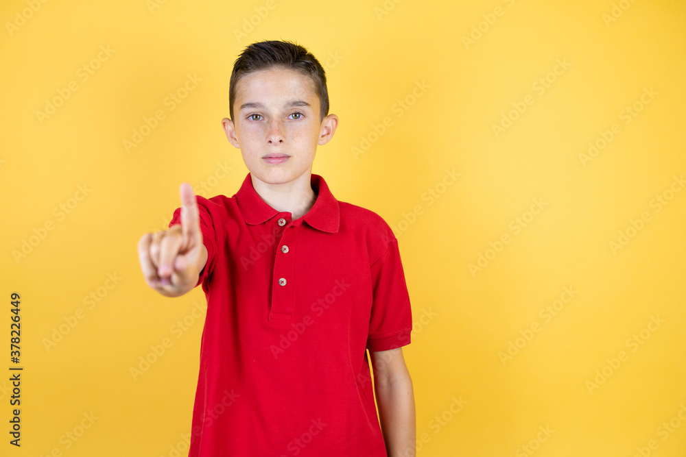 Young beautiful child boy over isolated yellow background showing and pointing up with fingers number one while is serious Young beautiful child boy over isolated yellow background showing and pointing up with fingers number one while is serious