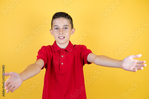 Young beautiful child boy over isolated yellow background looking at the camera smiling with open arms for hug