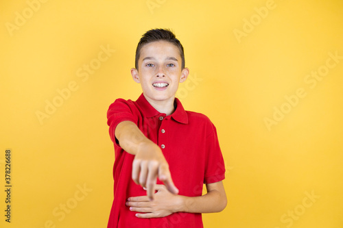 Young beautiful child boy over isolated yellow background laughing at you, pointing finger to the camera with hand over body, shame expression