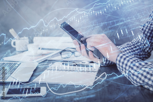 Double exposure of man's hands holding and using a digital device and forex graph drawing. Financial market concept.