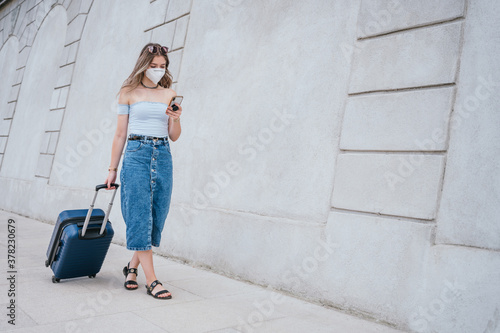 Tourist woman wearing mask walking with her suitcase through the city