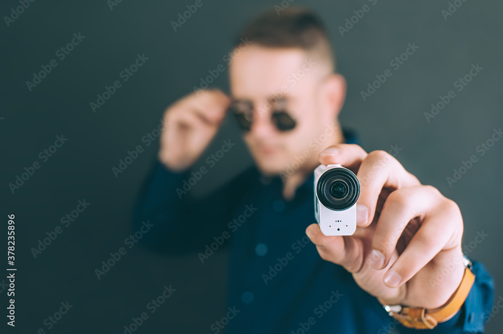 The guy takes photos, videos with an action camera, with one hand. on a black background in the studio. The guy takes photos, videos with an action camera, with one hand. on a black background in the studio.