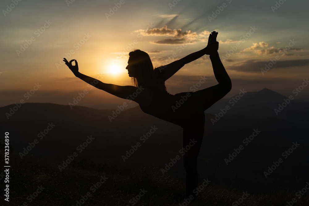 Silhouette of woman practice yoga on top of the mountain against a sunset - Concept of meditation stretching and relaxation