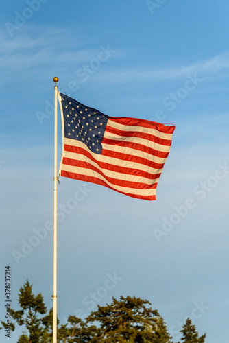 American flag blowing in the wind against a blue sky with wispy white clouds
