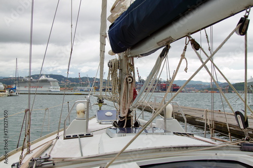 Closeup photo of the bow of a sailboat moored at the harbour with cruise ship in the background © Ivan