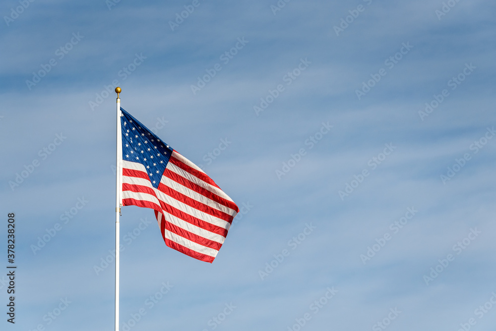 American flag blowing in the wind at sunset, against a blue sky with wispy white clouds
