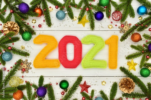 New year 2021, Christmas. Knitted colored numbers, fir branches and Christmas decorations on a white wooden background. Texture, design, decor, amigurumi, creativity, hobby, greeting card, handmade.