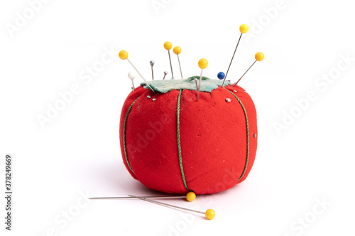 close up of a red pin cushion full of  straight pins and yellow quilt pins isolated on white photo