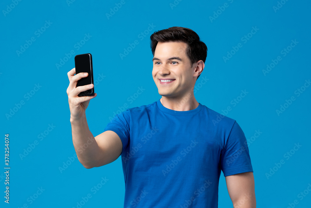 Portrait of smiling happy caucasian man taking a selfie with mobile phone in isolated studio blue background Portrait of smiling happy caucasian man taking a selfie with mobile phone in isolated studio blue background