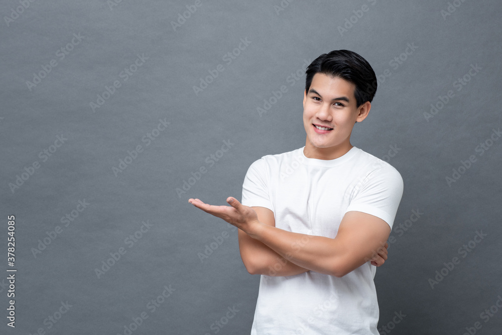 Product placement and advertising concept portrait of young Asian man smiling with palm open isolated on studio gray background Product placement and advertising concept portrait of young Asian man smiling with palm open isolated on studio gray background