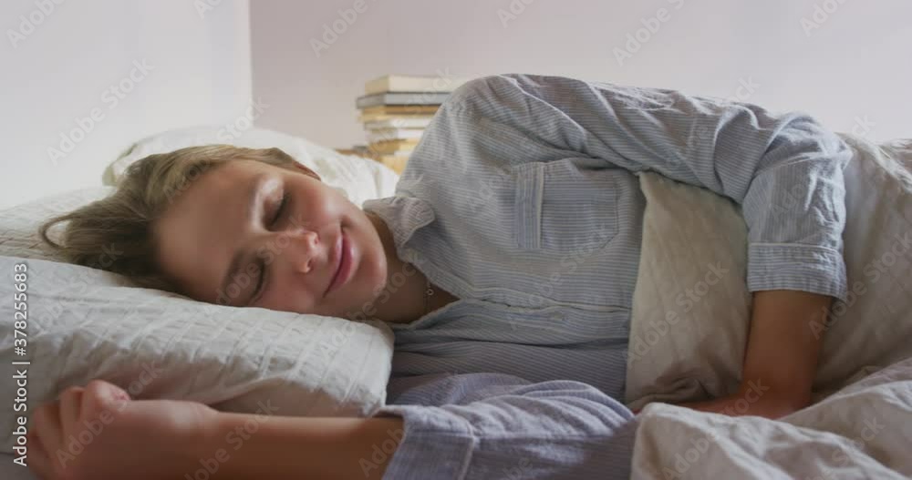 Authentic Shot of an Young Blond Woman is Waking up after Sleeping Peacefully and Comfortably Wrapped in a Warm Duvet Blanket in a Cosy Bed in a Bedroom in the Morning. Authentic Shot of an Young Blond Woman is Waking up after Sleeping Peacefully and Comfortably Wrapped in a Warm Duvet Blanket in a Cosy Bed in a Bedroom in the Morning.