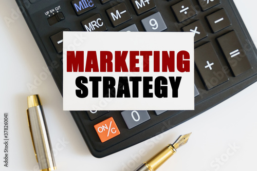 On the table there is a pen, a calculator and a business card on which the text is written - MARKETING STRATEGY