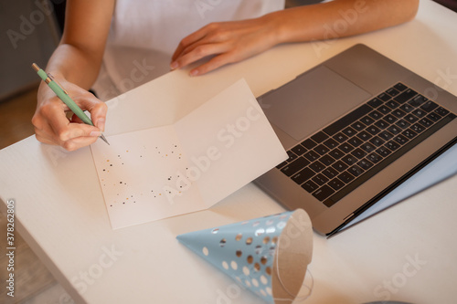 Young woman sitting at home at the table writes a greeting card. Birthday or anniversary concept