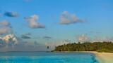 Golden hour in the Maldives. Sandy beach, turquoise ocean. Palm trees against the blue sky. Picturesque clouds.