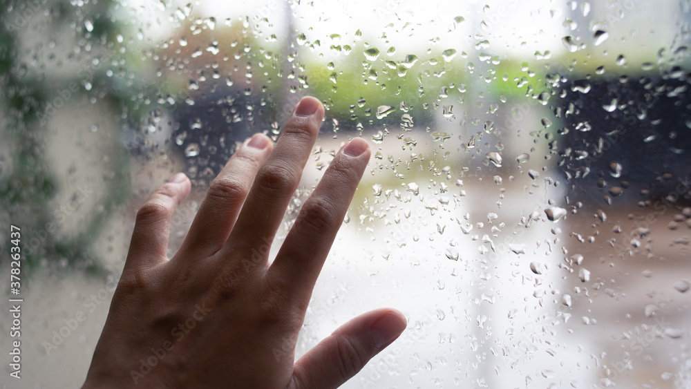 hand touching the window with rain drops with garden background