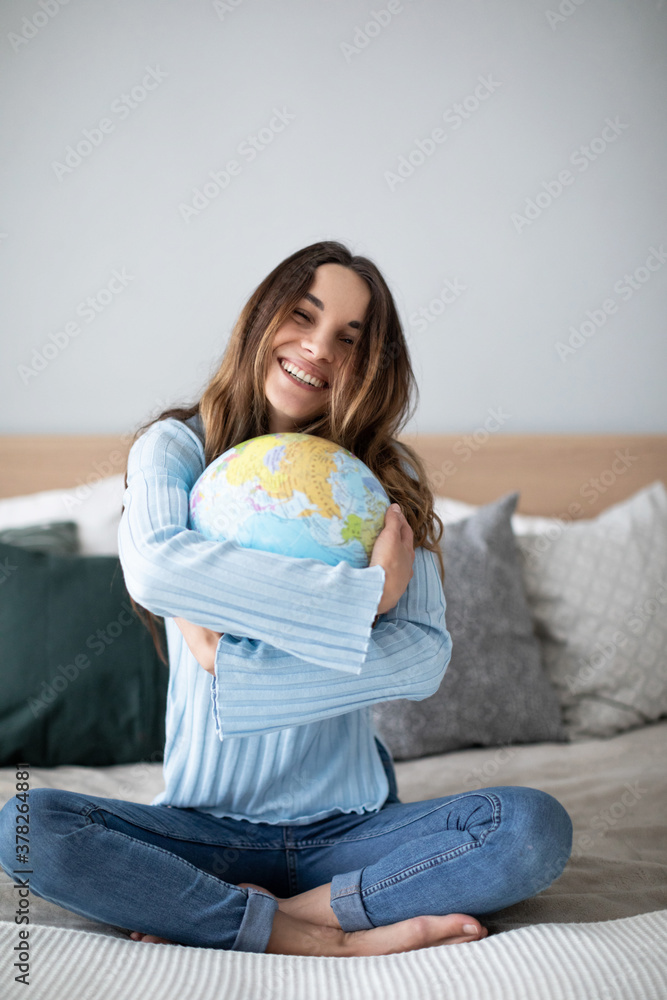 © BestForYou - Cheerful young woman hugging globe sitting on the couch at home.