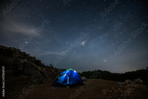 A tent glows under a night sky full of stars.
