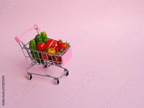Pink shopping cart full of vegetables on pink background