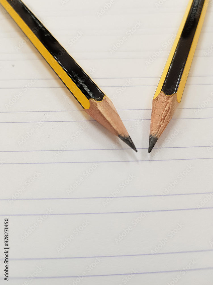 Two sharpened pencil over a ruled white paper Two sharpened pencil over a ruled white paper