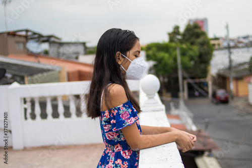 Niña latina con protección mascarilla pensando desde su balcón © JuanCarlos
