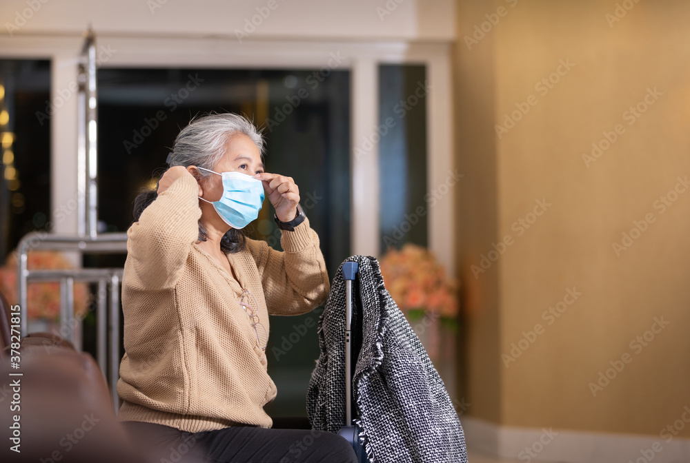 one mature woman wearing medical mask with his luggage or trolley travelling at the hotel - senior waiting his friend preventing coronavirus or another type of virus (covd-19) one mature woman wearing medical mask with his luggage or trolley travelling at the hotel - senior waiting his friend preventing coronavirus or another type of virus (covd-19)