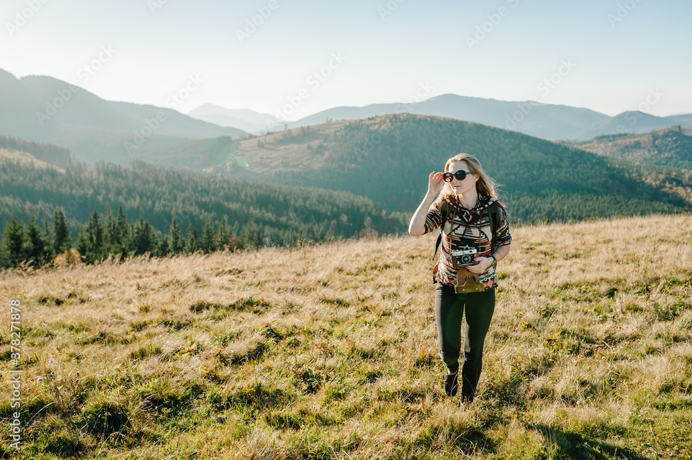 Hiker tourist in the mountains at sunset. Girl takes pictures of the sunrise. Hipster girl with a photo camera and a backpack travels and enjoy nature. Hiker tourist in the mountains at sunset. Girl takes pictures of the sunrise. Hipster girl with a photo camera and a backpack travels and enjoy nature.