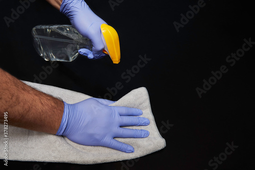 Gloved man hands cleaning a table with a spray cleaner and rag