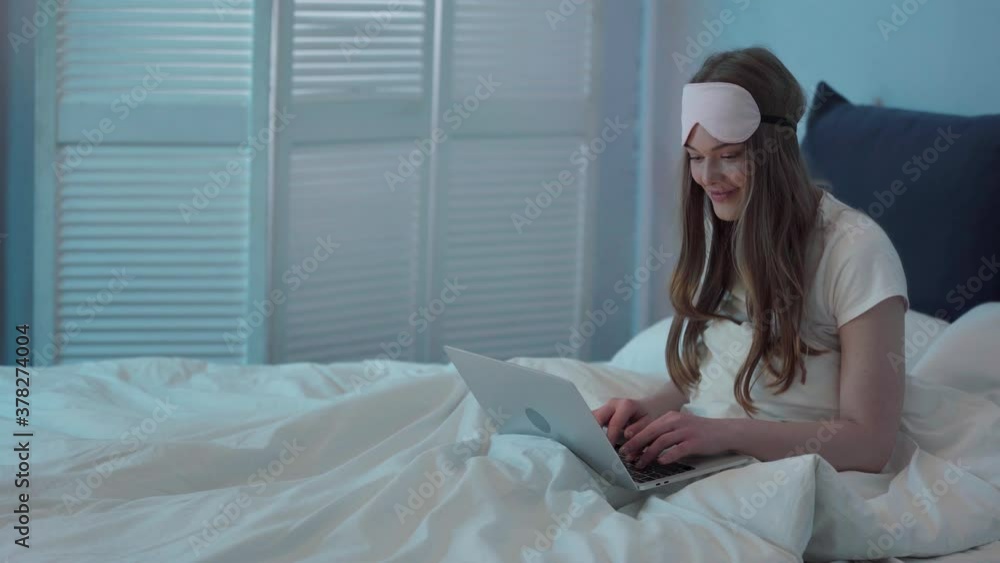 Young woman sitting in bed and typing on laptop Young woman sitting in bed and typing on laptop