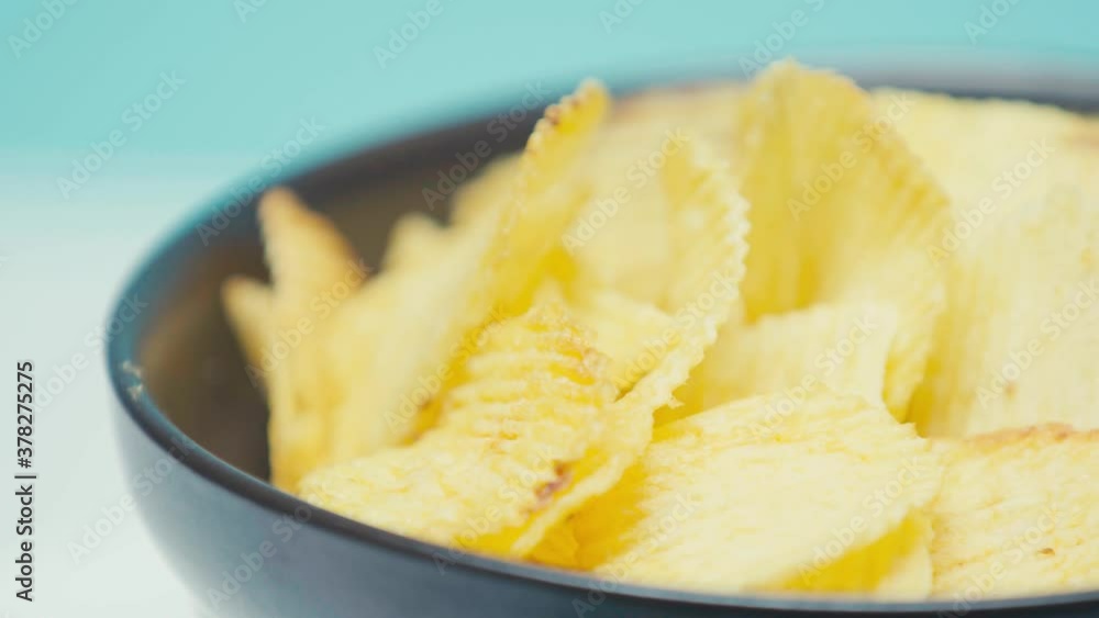 Close up view of ridged chips in black bowl spinning on blue background Close up view of ridged chips in black bowl spinning on blue background