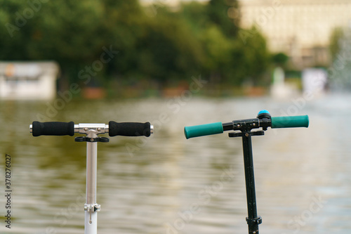 Photography of two parked push scooters near fountain in the public park of Moscow. Traveling and leisure concept.