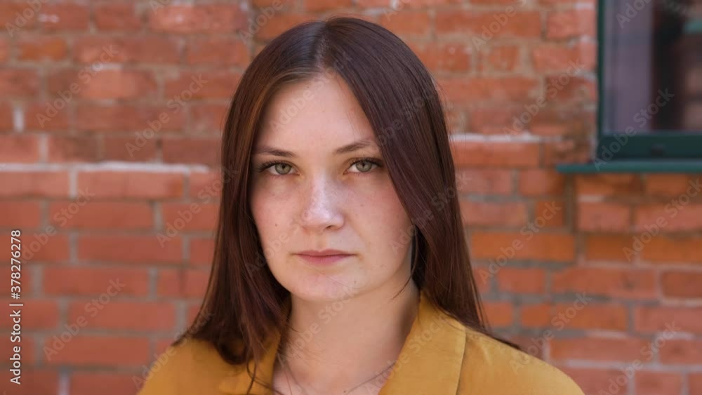 Beautiful girl with brown, red long hair stands in a yellow shirt against background of brick office under window. Looking at camera, sad, bad mood, bad luck work, disappointment, difficult choices Beautiful girl with brown, red long hair stands in a yellow shirt against background of brick office under window. Looking at camera, sad, bad mood, bad luck work, disappointment, difficult choices