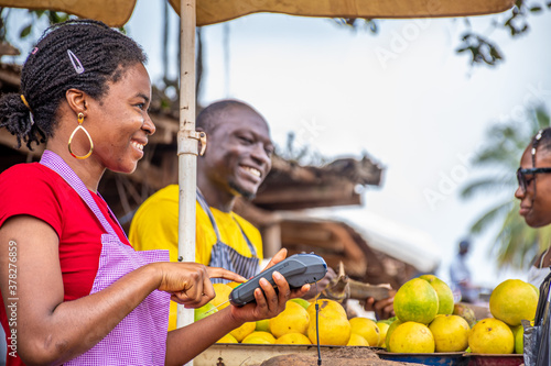 african woman using a pos machine in a market smiling, other people in the background trading photo