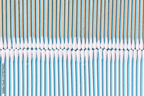 Comparison of cotton swabs with eco friendly wooden stick on one side and plastic stick on other side of blue background