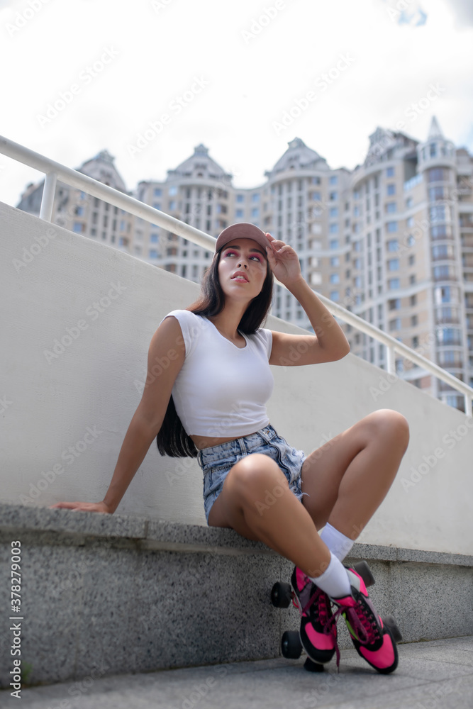 Fit girl in jeans shorts in roller-skates sitting on street curb