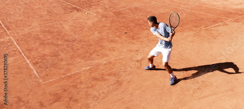 Tennis player playing on clay court. Young male tennis player hitting backhand kick. Professional athlete is concentrating in the game. Sports background. Banner. Copy space for text © Elena