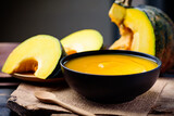 Pumpkin soup in a bowl with spoon and fresh pumpkins on wooden table
