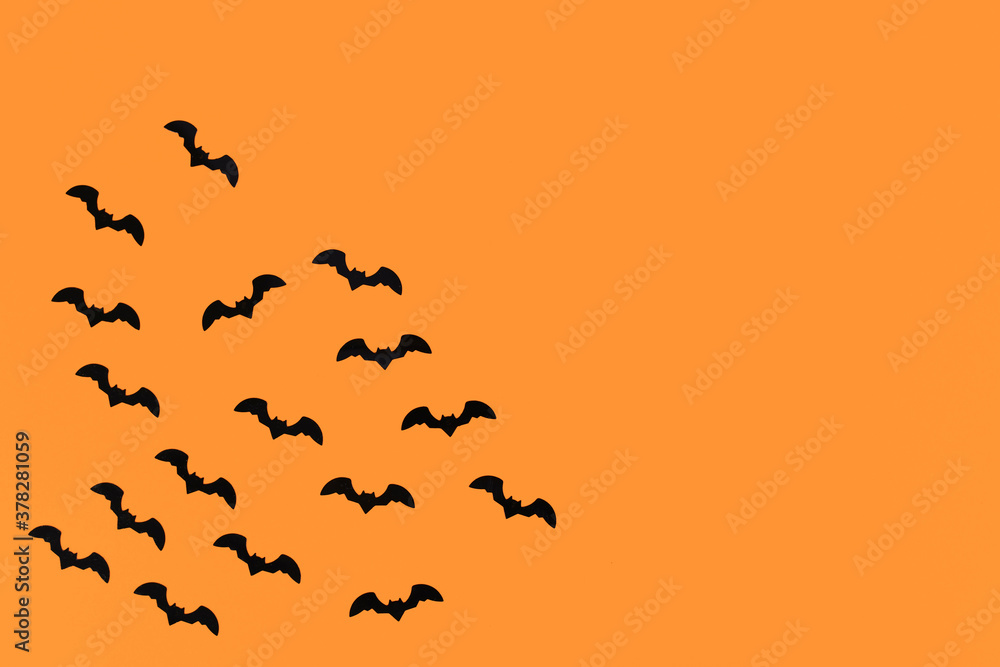 Seasonal Halloween deco confetti in shape of small flying black bats in corner of orange background with empty copy space Seasonal Halloween deco confetti in shape of small flying black bats in corner of orange background with empty copy space