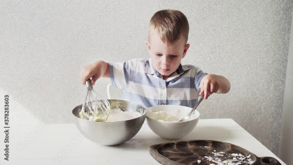 Young preschool boy cooking dough for cake by himself standing alone on white kitchen at home. Young preschool boy cooking dough for cake by himself standing alone on white kitchen at home.
