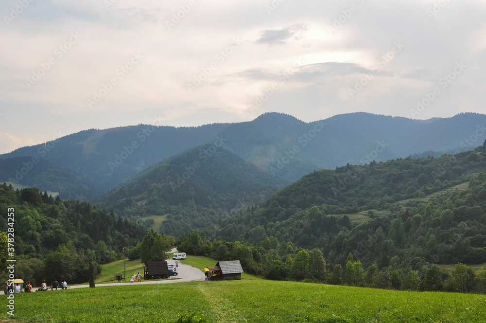 VLKOLINEC, SLOVAKIA, EUROPE, SUMMER. Beautiful views from the fantastic village of Vlkolinec which is a Unesco Heritage. In them you can see a road surrounded by green mountains and a wooden house.