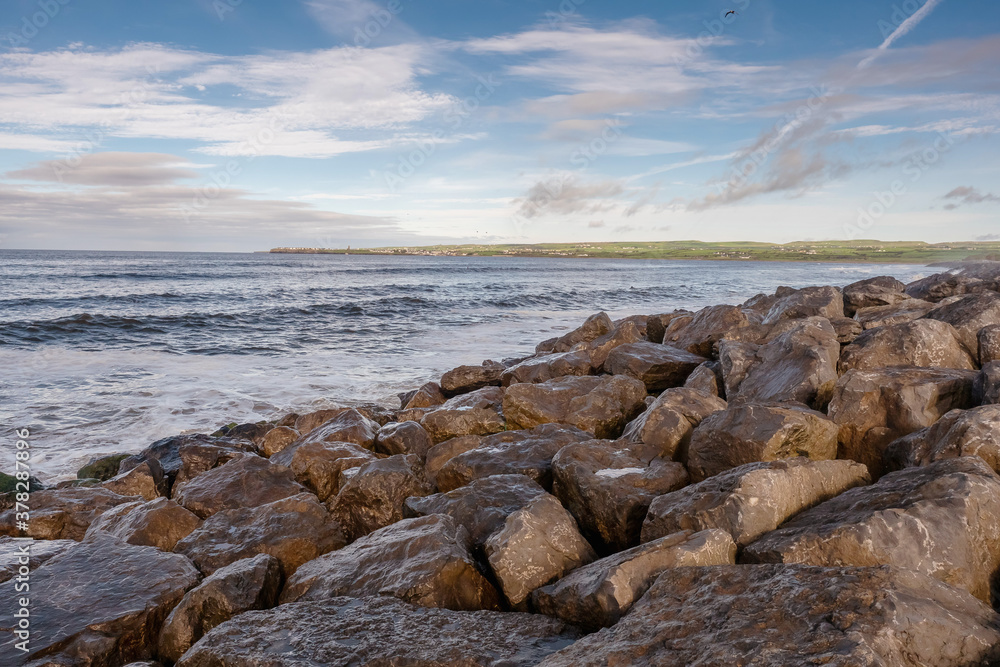 Rocks on a shore and Atlantic ocean, Lahinch town, county Clare, Ireland, Warm sunny day with cloudy sky. Nobody.
