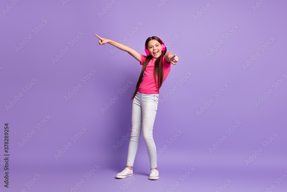 Full length body size photo of funky schoolgirl smiling listening to music singing like a pop star pointing with fingers isolated on purple color background Full length body size photo of funky schoolgirl smiling listening to music singing like a pop star pointing with fingers isolated on purple color background