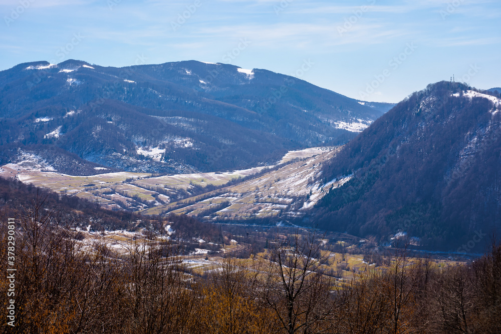 mountainous countryside in early spring. dry grass and leafless trees on the hillside. snow in the distant valley and ridge