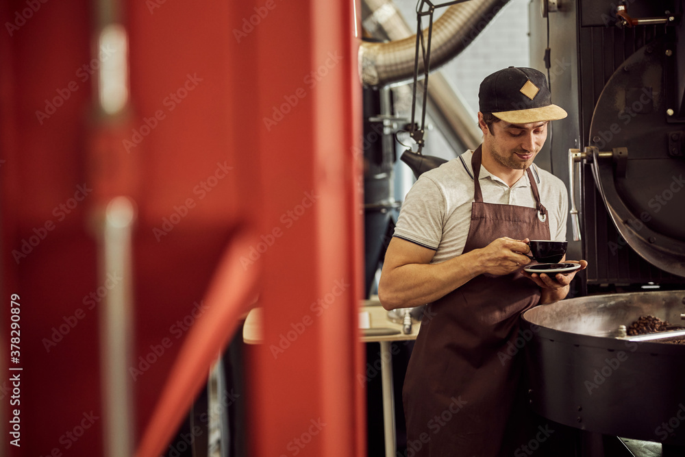 Handsome male worker in apron drinking coffee
