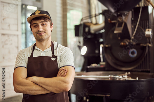 Handsome young man standing near coffee roasting machine
