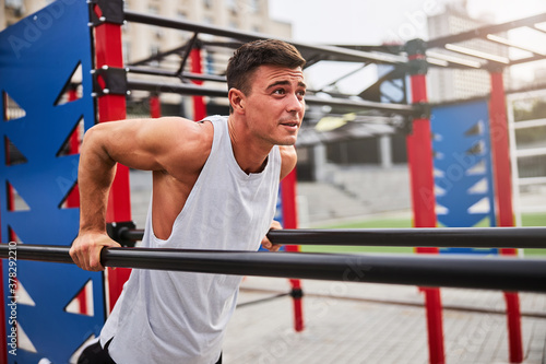 Cheerful young man doing pull ups outdoors